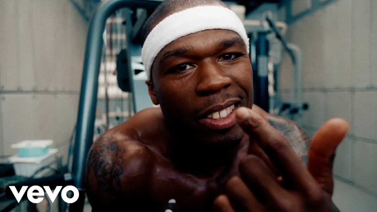 「In Da Club」MVの50 Cent。白いヘッドバンドを着け、研究施設風の室内にいる。