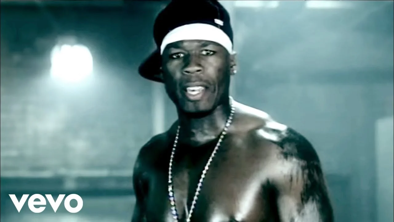 「Many Men (Wish Death)」MVの50 Cent。暗い帽子、白いヘッドバンド、背後に光と煙。