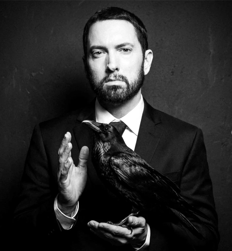黒いスーツ姿のEminemが、両手で黒いカラスを支えている。