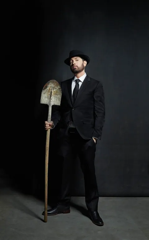 黒いスーツと帽子を身につけ、シャベルを持つEminem。Danny Clinch撮影。